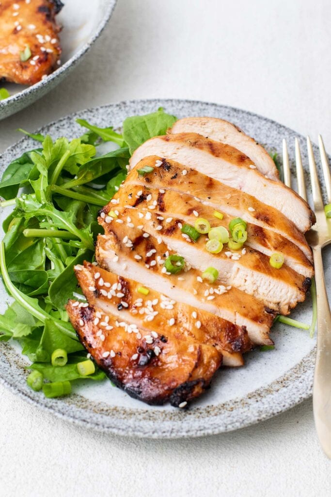 A sliced grilled chicken breast over an arugula salad.