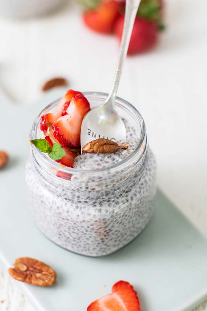 A jar of keto chia pudding topped with strawberries with a spoon taking a bite.