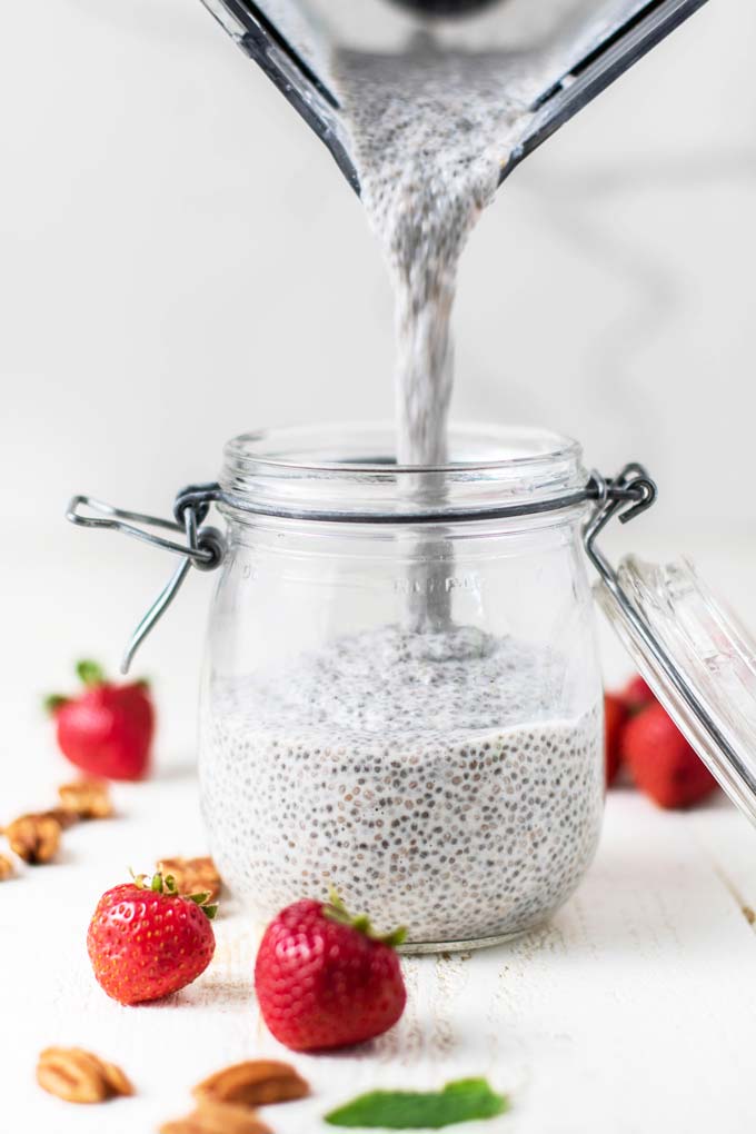 A blender jar pouring chia pudding into a large storage jar.