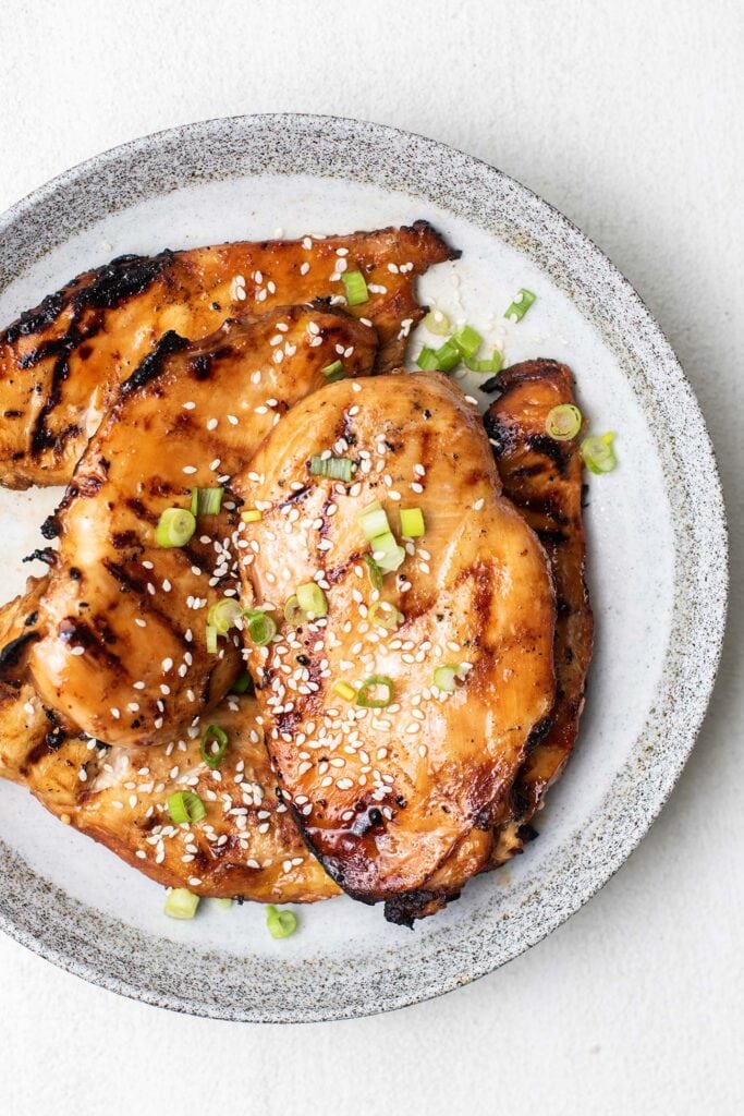 A plate of marinated grilled chicken breasts garnished with chopped green onions.