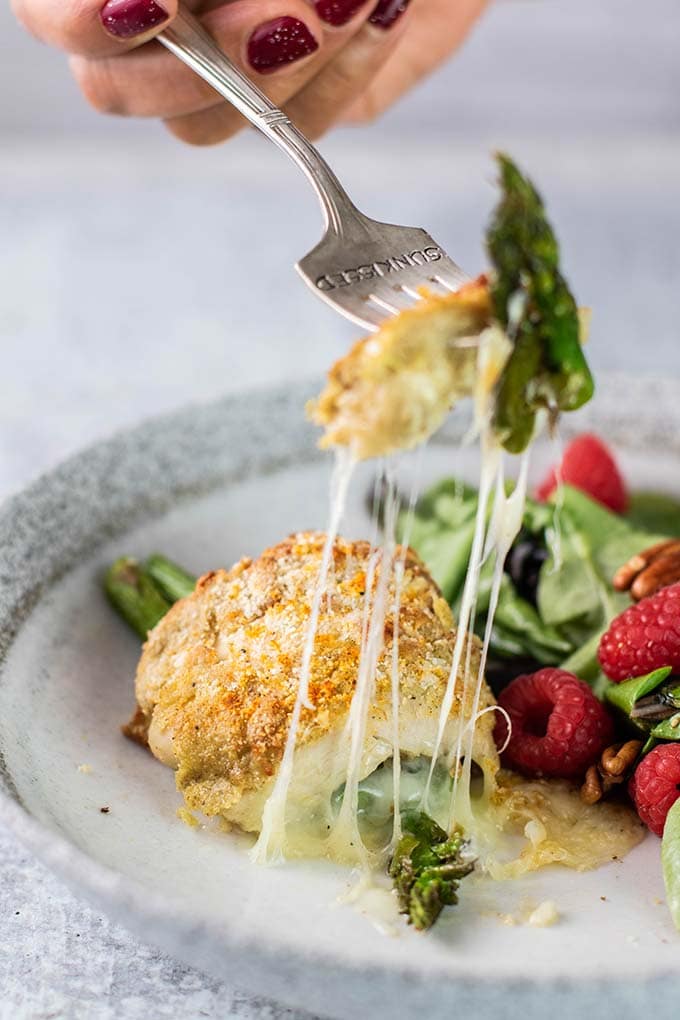 A fork pulling a bite of asparagus stuffed chicken, with strings of cheese.