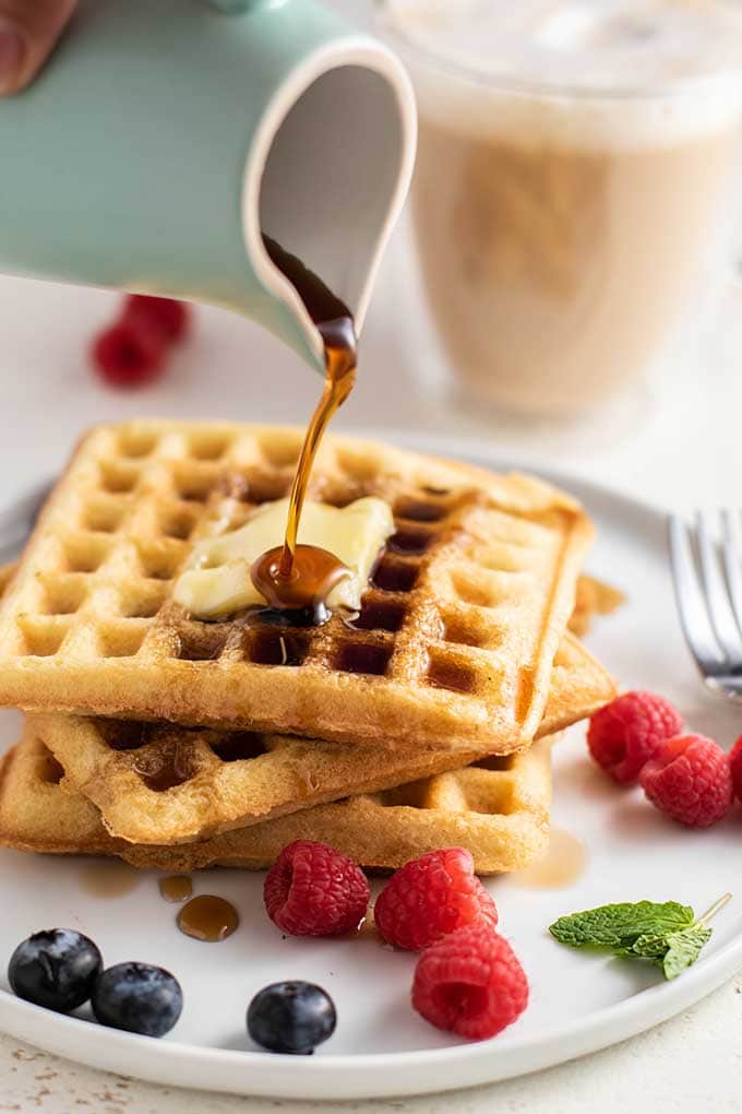 Syrup being poured on a stack of almond flour waffles with melted butter.