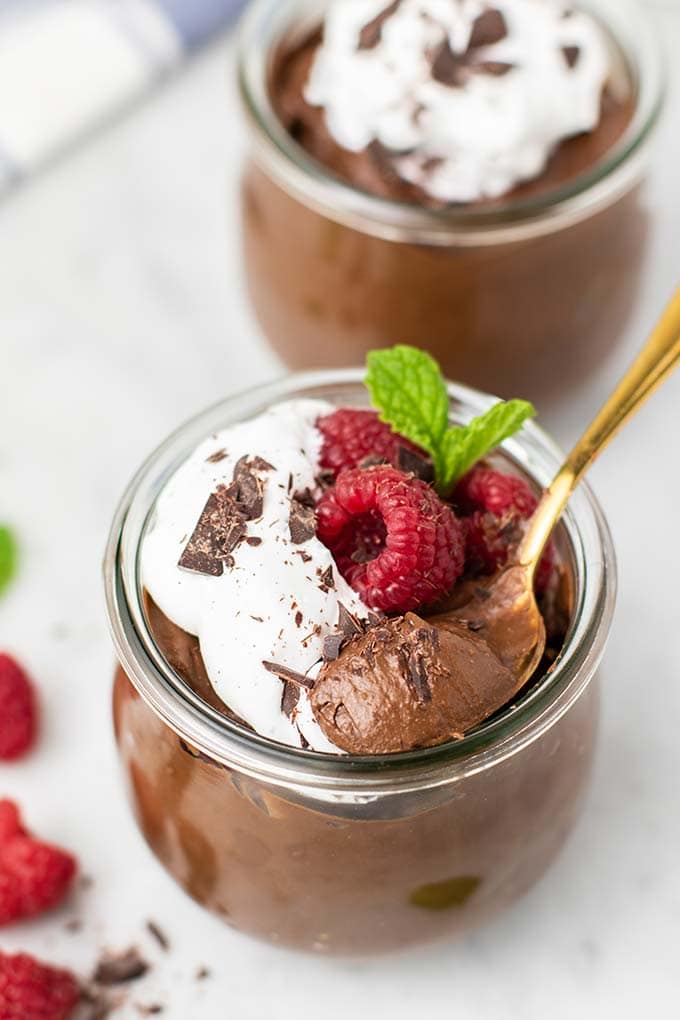 A close up photo of a jar of chocolate avocado pudding, with a spoon taking a bite out of the jar.