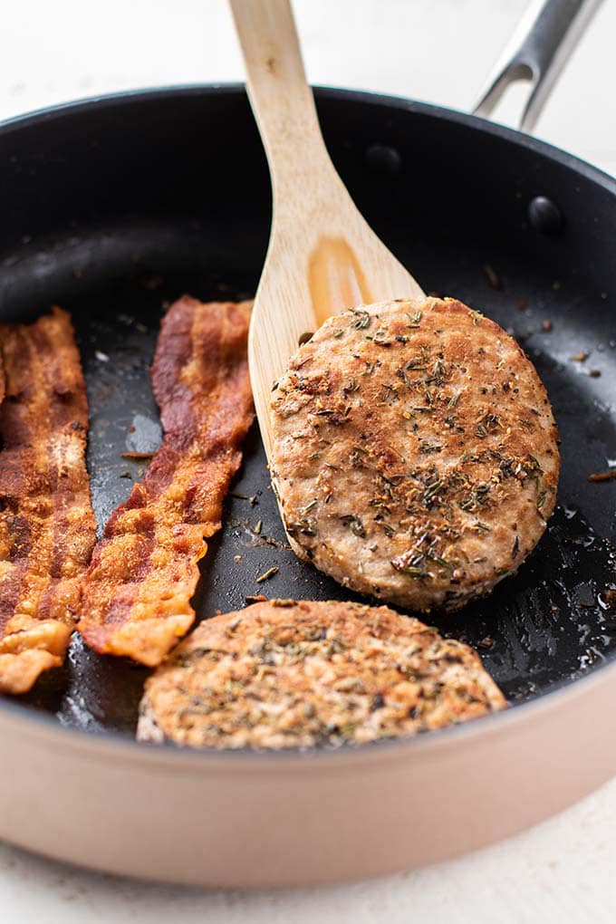 Two turkey burgers and bacon frying in a pan.