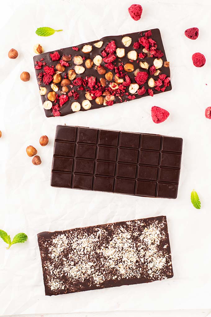 Three dark chocolate bars, one plain, one with raspberries and hazelnuts, and one with toasted coconut.