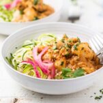 A side view of a bowl layered with cauliflower rice and a keto butter chicken with pickled onions.