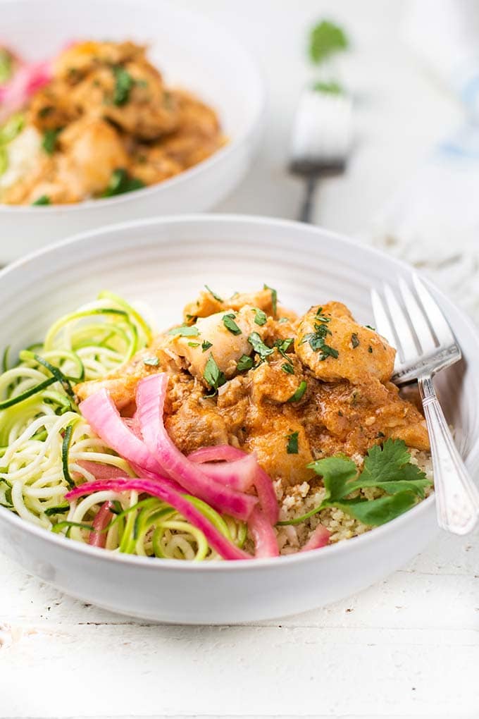 A side view of a bowl layered with cauliflower rice and a keto butter chicken with pickled onions.