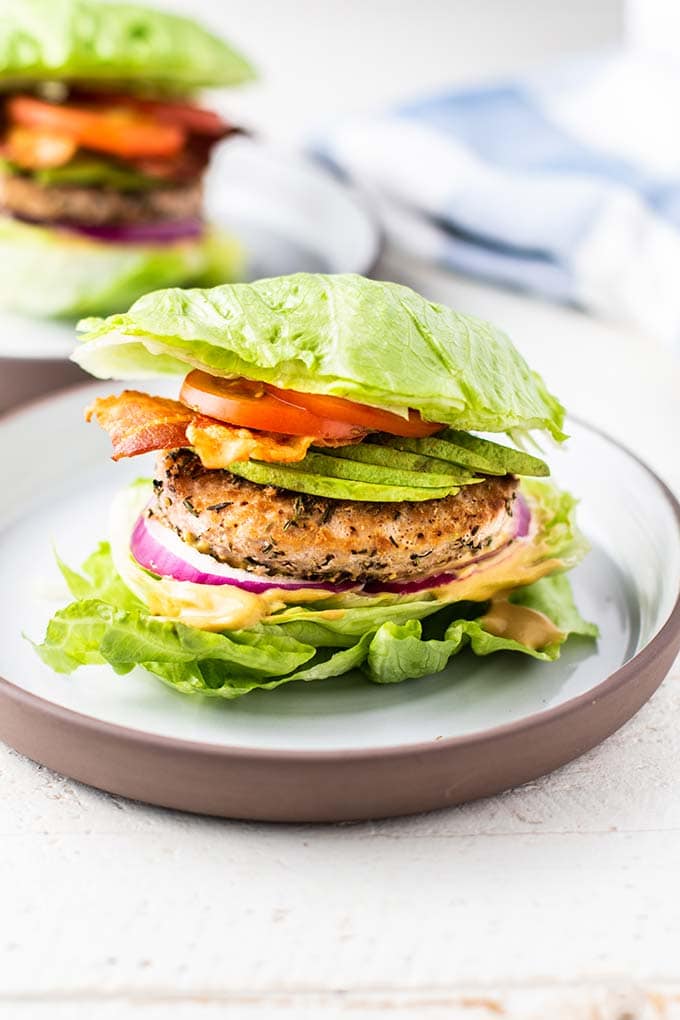 A turkey burger with avocado between two chunks of lettuce.