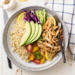 A white plate with cauliflower rice, shredded instant pot chicken thighs, tomatoes, cabbage and avocado.