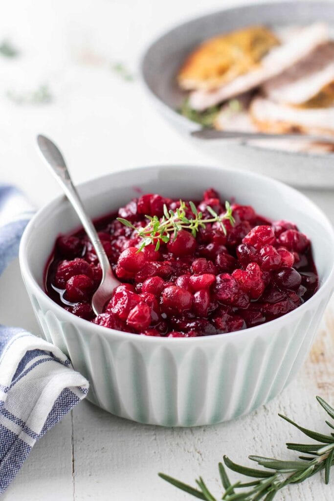 A blue bowl with cranberry sauce, with a silver spoon.
