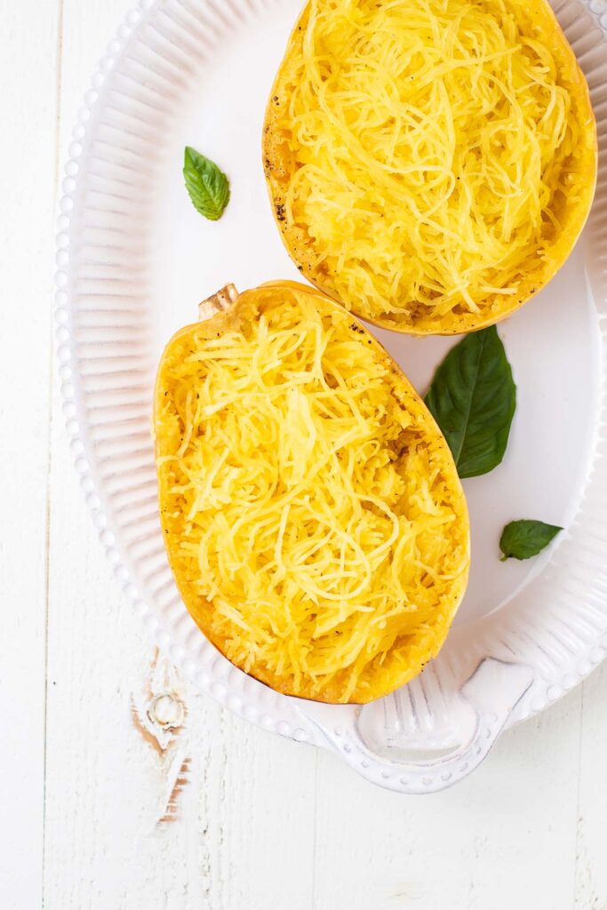 A spaghetti squash baked with the strands pulled away from the shell shown on a serving platter.