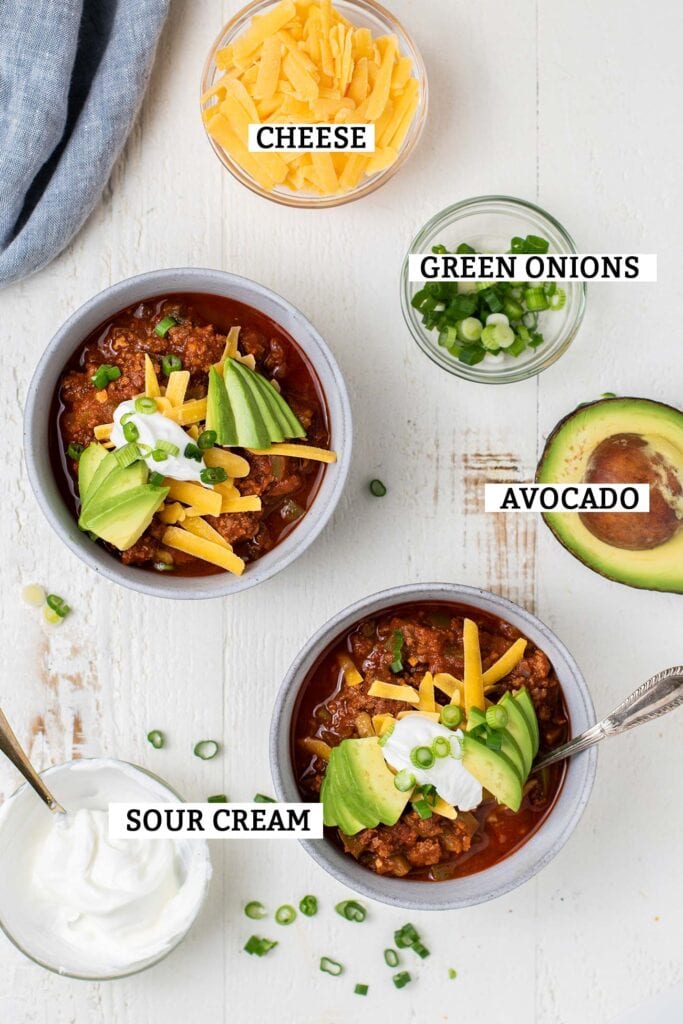 Two bowls of chili surrounded by topping suggestions with labels.