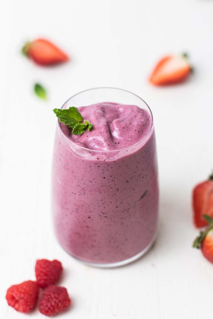 A clear glass with an acai smoothie garnished with mint leaves and strawberries.