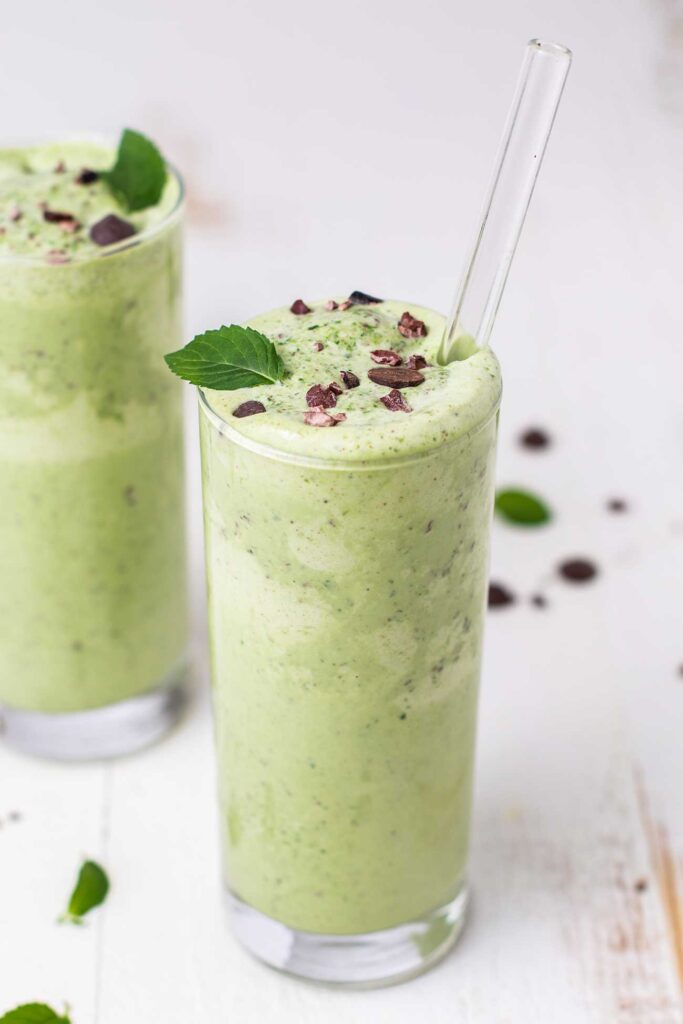 Two mint chocolate chip keto smoothies in glasses garnished with cocoa nibs and mint leaves.