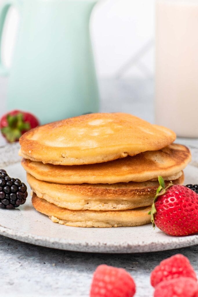 A stack of golden brown low carb pancakes on a plate next to a container of sugar free maple syrup.