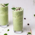 Two keto smoothies shown in tall glasses garnished with cocoa nibs and mint leaves.