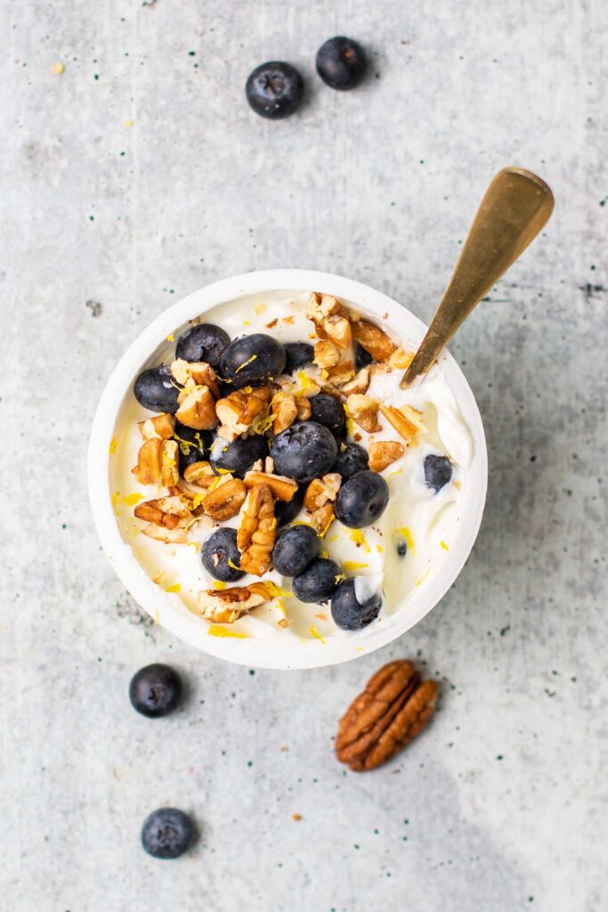A Greek yogurt topped with blueberries, lemon zest, and pecans.