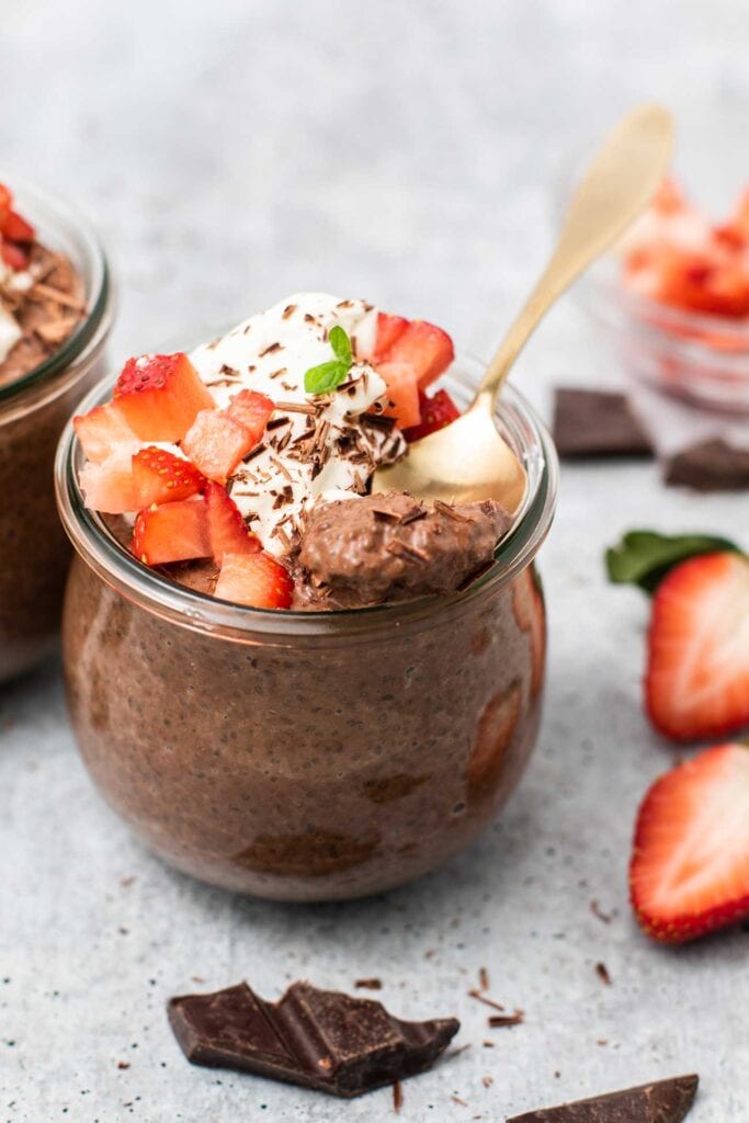 A jar with chocolate chia seed pudding, topped with whipped cream and strawberries.
