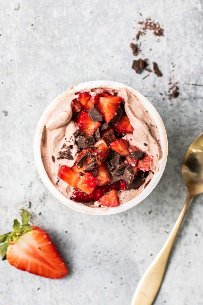 A close up look at a Greek yogurt with chocolate and strawberries added to it.