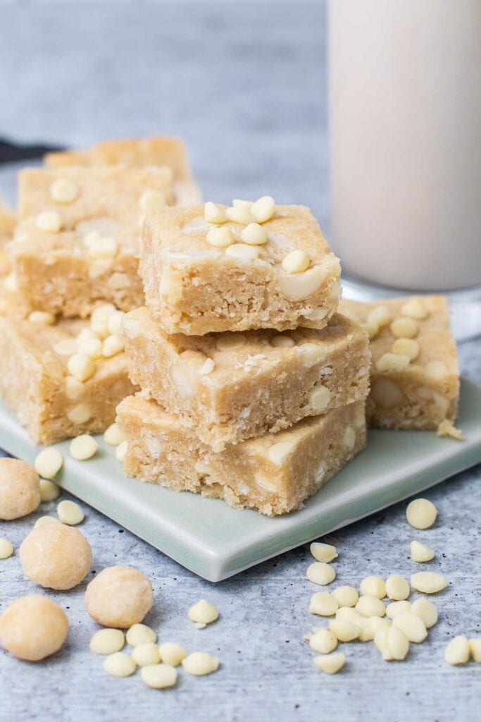 White chocolate chip and macadamia nut cookie bars stacked in front of a glass of milk.