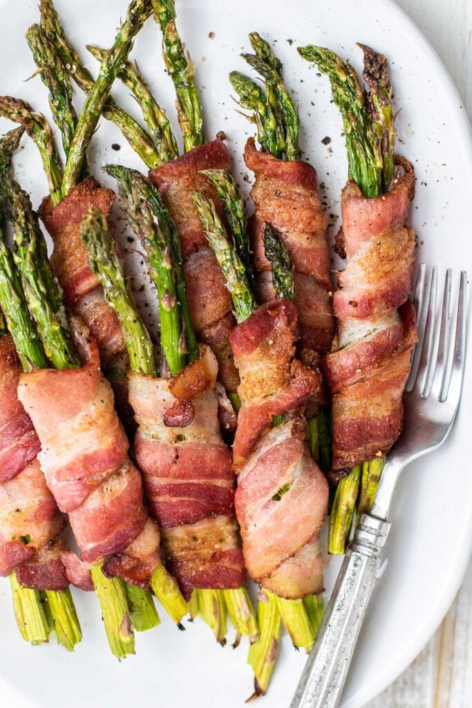 A close up look at bundles of asparagus wrapped in crispy bacon served on a white plate.