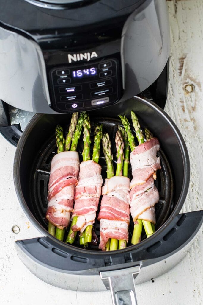 A Ninja Air fryer shows with bacon wrapped asparagus.