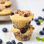 Two blueberry muffins stacked on top of each other surrounded by blueberries.