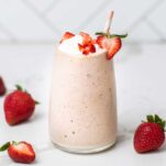 A keto strawberry smoothie shown with a straw and garnished wtih whipped cream.