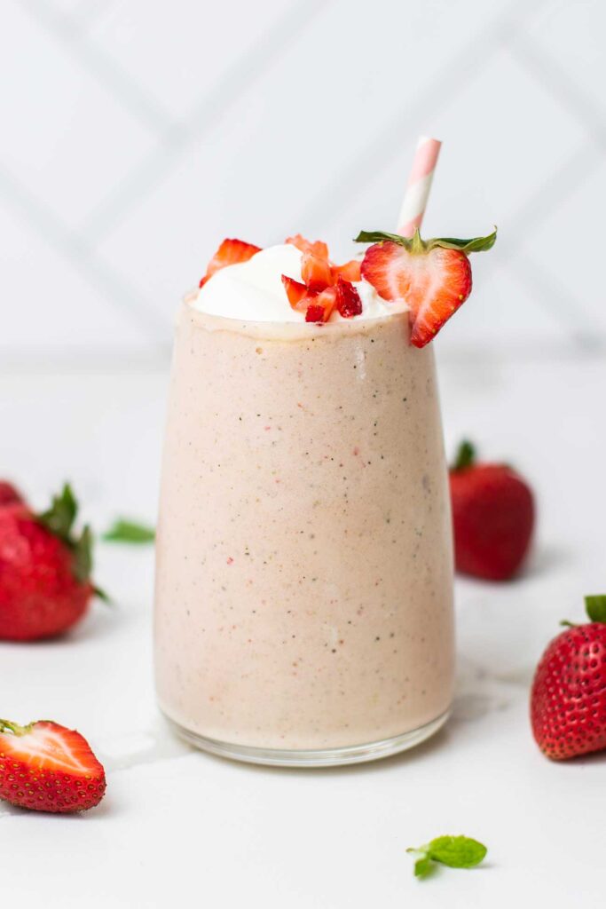 A keto strawberry smoothie shown garnished with whipped cream and chopped strawberries.