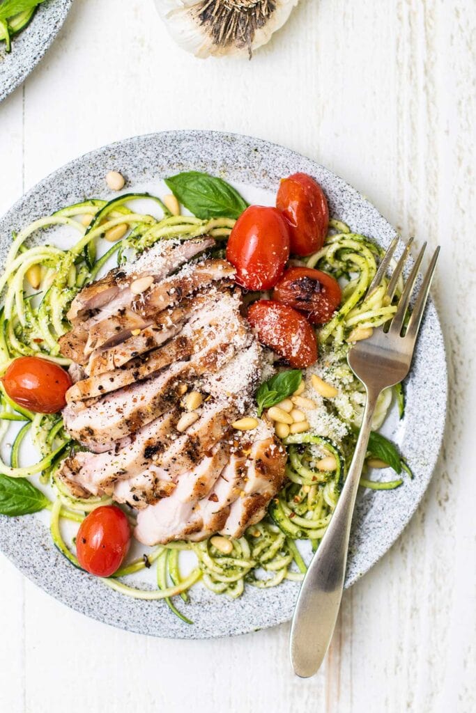 A plate with pesto zoodles topped with an herb marinated chicken thigh.