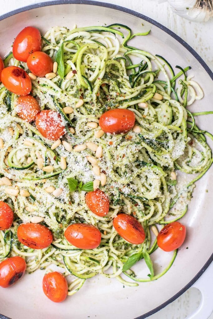 A white pan with zoodles tossed in pesto garnished with cherry tomatoes.