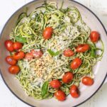 A large white pan shown with pesto zoodles garnished with burst cherry tomatoes.