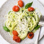 A bed of zucchini noodles topped with parmesan cheese, basil, and tomatoes.