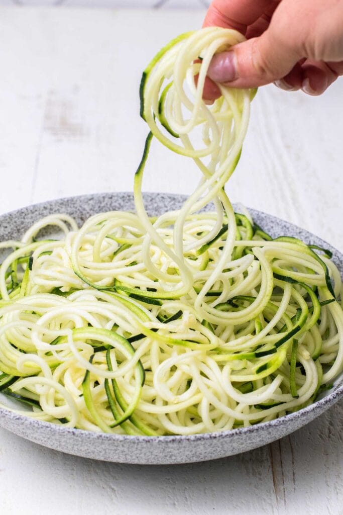 Zoodles in a dish being pulled up to show the even strands.