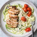 A plate of zoodles in a creamy alfredo sauce topped with chicken.