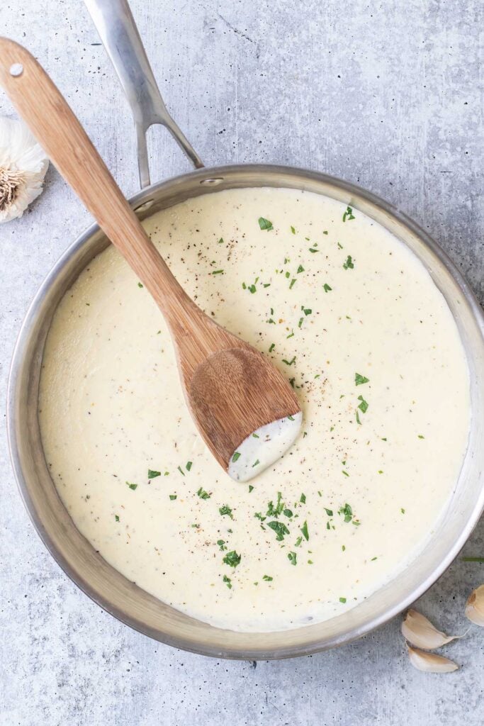 A creamy alfredo sauce shown in a skillet garnished with parsley.