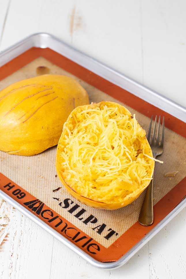 Spaghetti squash shown on a baking pan with the strands pulled away from the skin.
