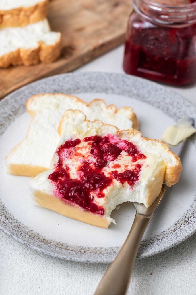 Two slices of zero carb bread on a plate with butter and raspberry jam.