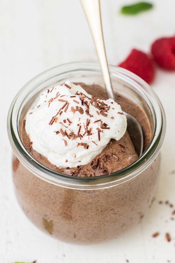A jar of creamy smooth chia pudding topped with whipped cream and shaved dark chocolate.