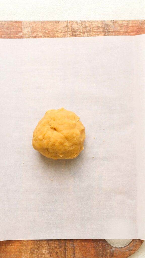 An orange ball of keto cheese cracker dough sitting on a piece of parchment paper.