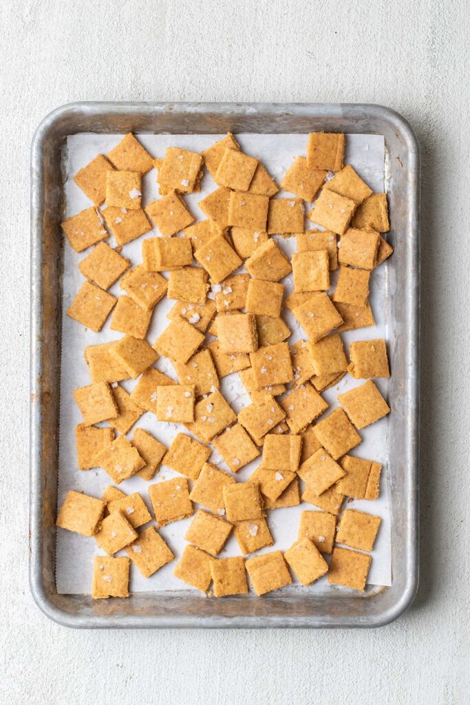 A baking pan with keto cheese crackers broken into 1 inch squares, looking like Cheez Its.