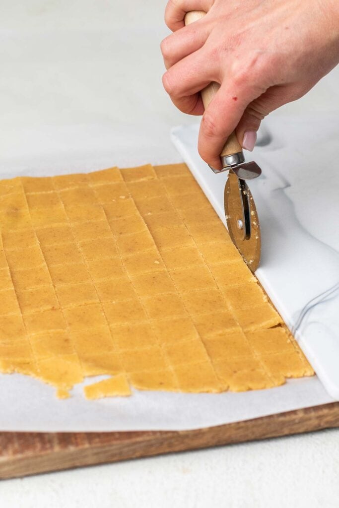Cheese cracker dough being cut into squares with a pizza cutter.