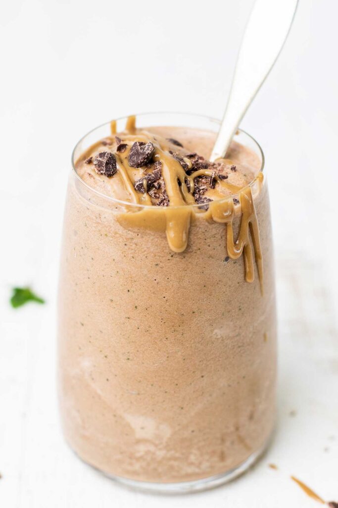A CHOCOLATE PEANUT BUTTER SMOOTHIE SHOWN DRIZZLED WITH PEANUT BUTTER AND DARK CHOCOLATE SHAVINGS.