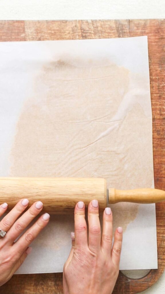 Cracker dough being rolled out between two layers of parchment paper.