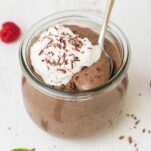 A jar of creamy blended chia seed pudding shown topped with whipped cream and shaved chocolate.