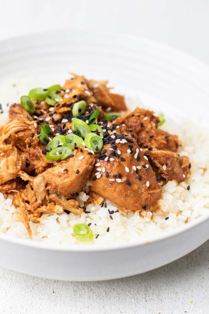 A plate of crockpot asian chicken served over a bed of cauliflower rice.