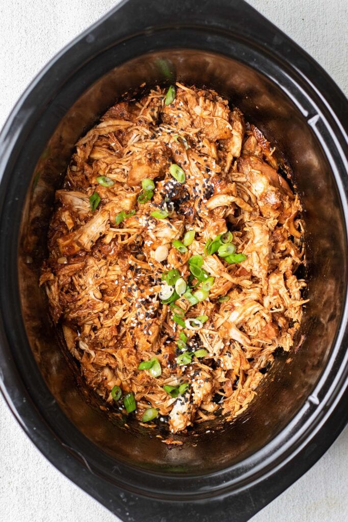 Chicken in a crockpot garnished with green onions and sesame seeds.