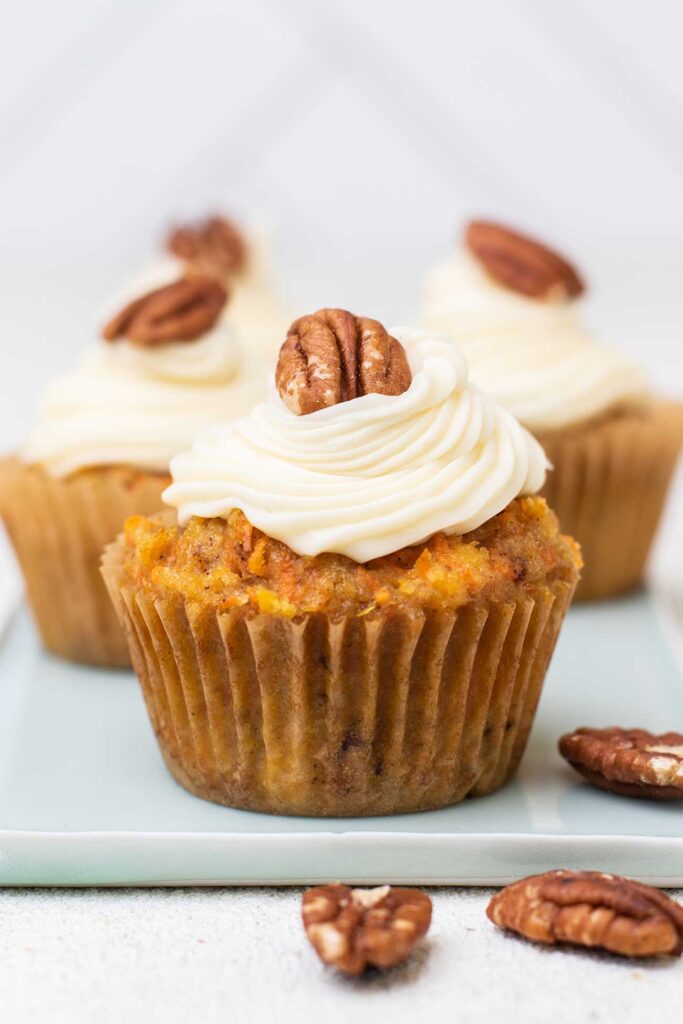 Keto carrot cake cupcakes topped with fluffy cream cheese frosting and a pecan.