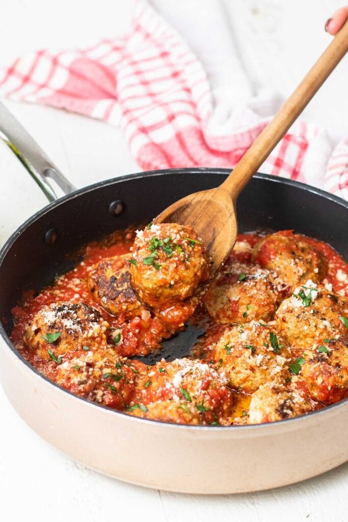 Meatball being heated in a skillet with marinara sauce.