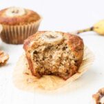 A banana muffin shown sitting on a counter with a banana and some walnuts.